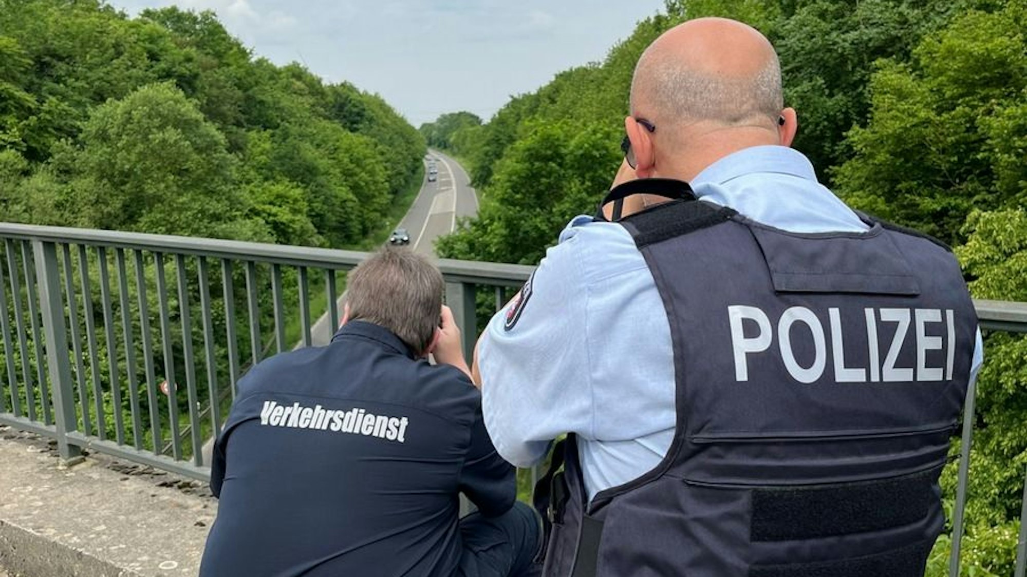 Auf dem Foto sind zwei Polizeibeamte zu sehen, die von einer Brücke aus die Geschwindigkeit der Verkehrsteilnehmer auf der B 59 messen.