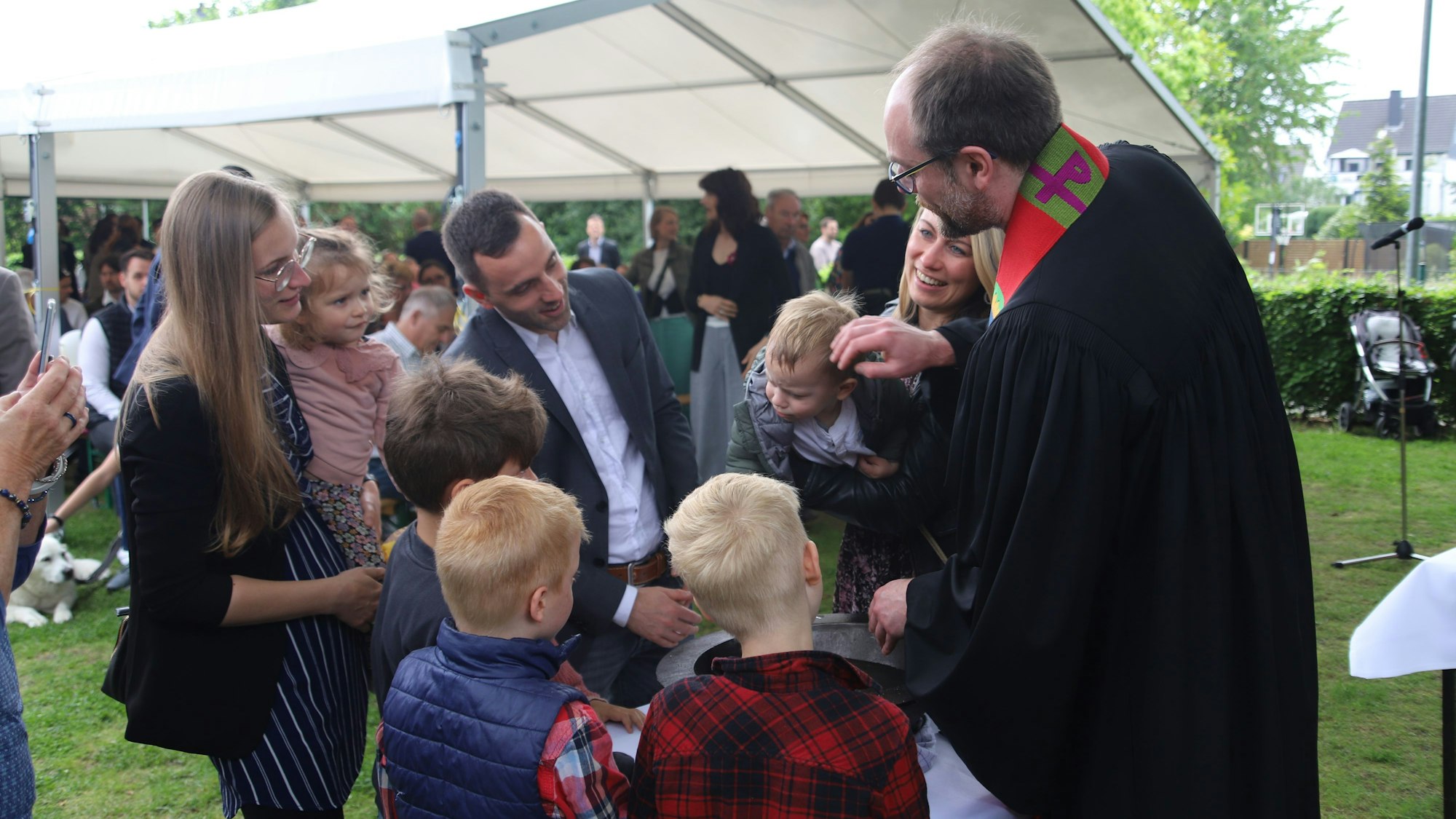 Ein Pfarrer beträufelt den Kopf eines Täuflings im Kreis der Familie.