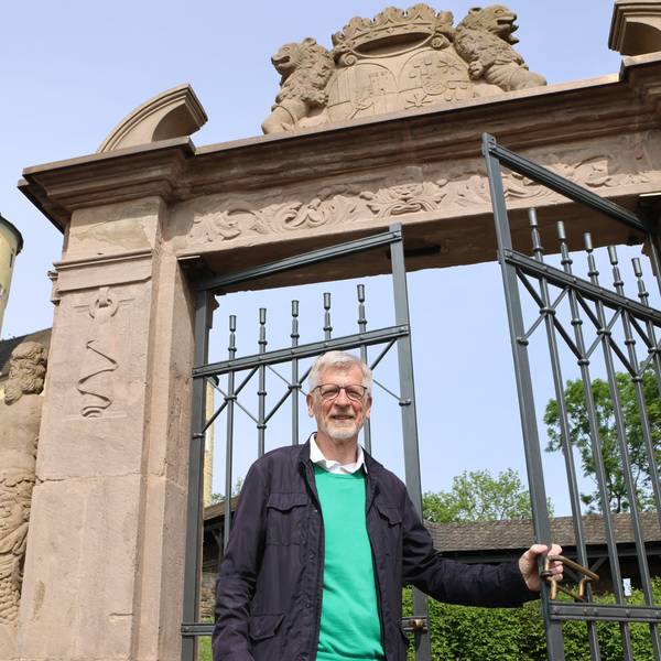 Ein Mann steht an einem Metalltor, dahinter ragt der Schlossturm auf.