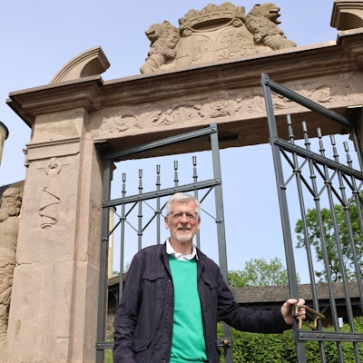 Ein Mann steht an einem Metalltor, dahinter ragt der Schlossturm auf.