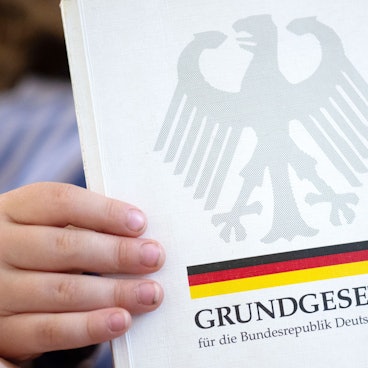 ARCHIV - 13.05.2024, Sachsen, Leipzig: ILLUSTRATION - Ein kleine Junge hält eine Ausgabe des Grundgesetzes in seinen Händen.