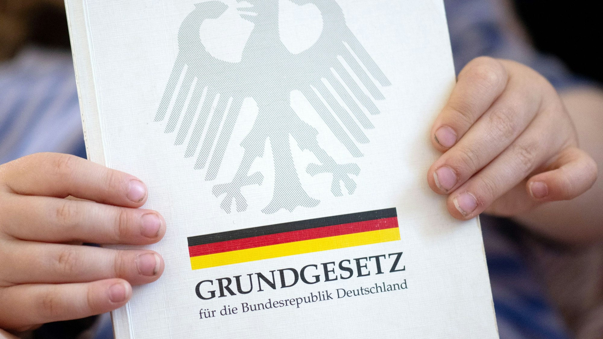 ARCHIV - 13.05.2024, Sachsen, Leipzig: ILLUSTRATION - Ein kleine Junge hält eine Ausgabe des Grundgesetzes in seinen Händen.