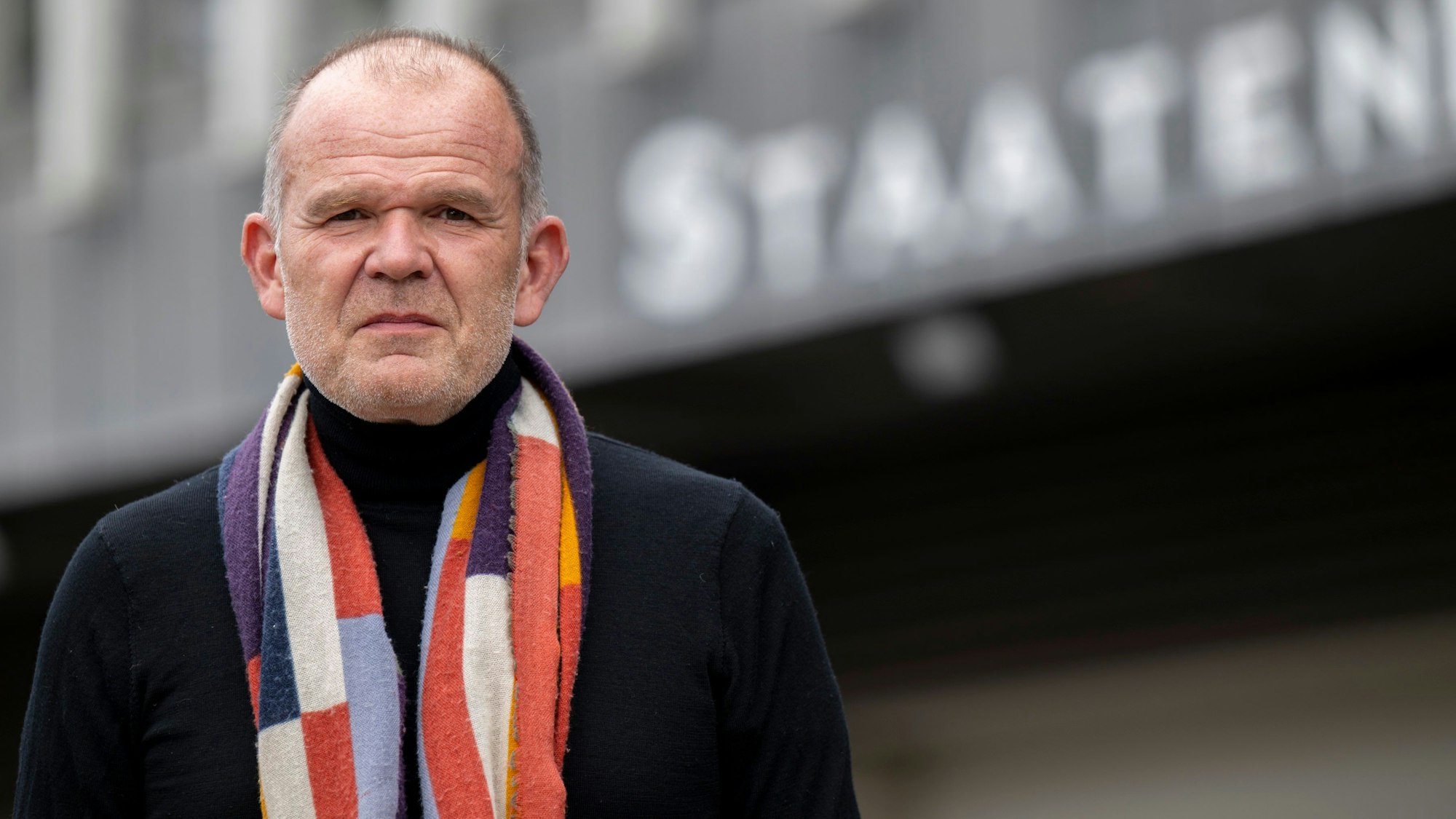 François-Xavier Roth steht vor dem Staatenhaus. Er trägt einen bunten Schal.