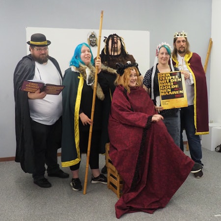 Sechs junge Erwachsene in Kostümen spielen Theater.