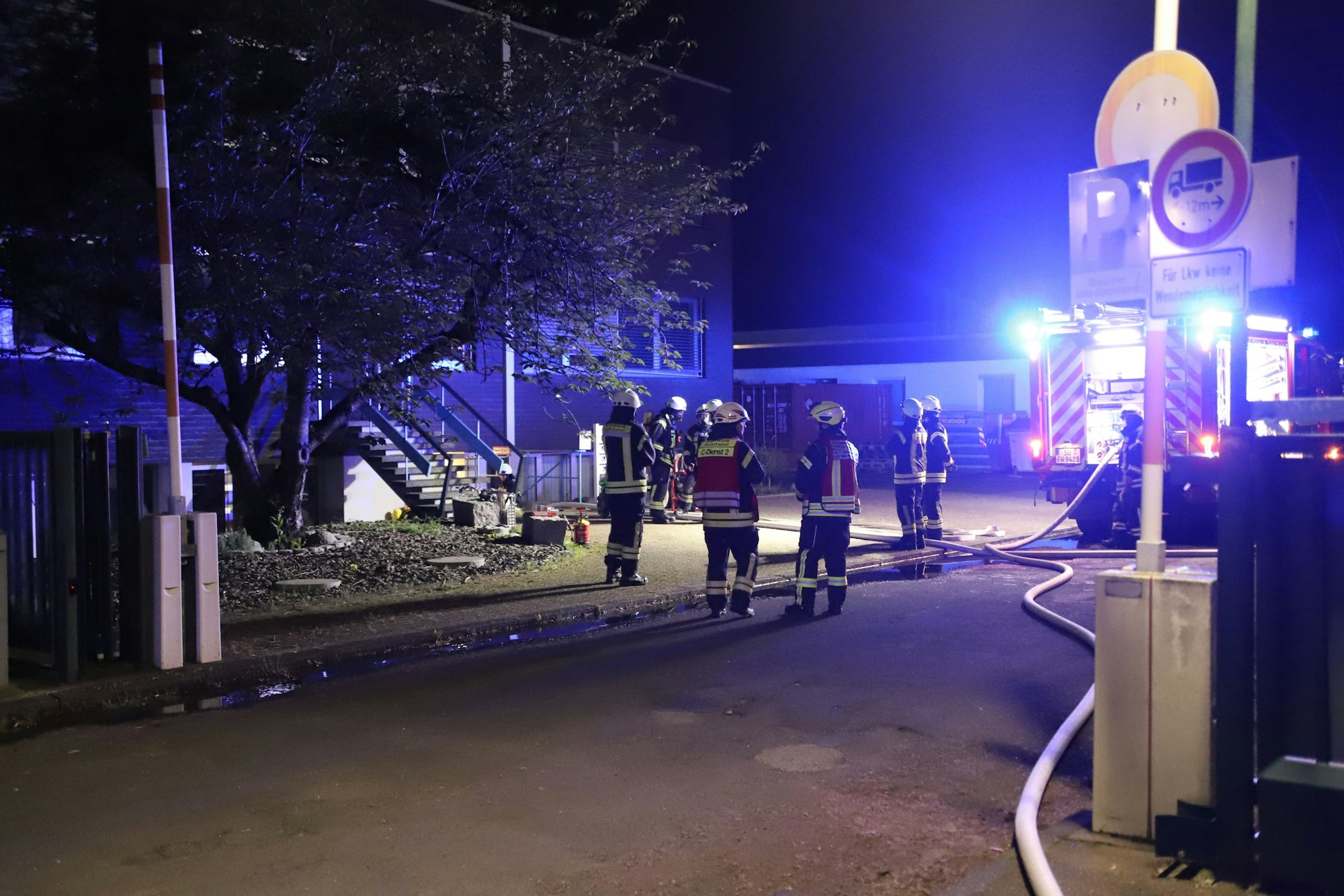 Feuerwehrleute stehen vor den Gebäuden eines Maschinenbauunternehmens und haben Wasserschläuche verlegt.