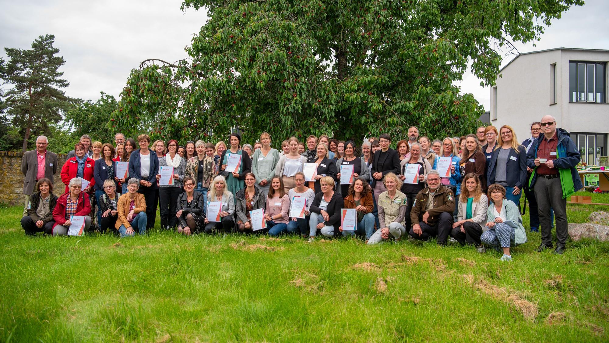 Eine Gruppe von Menschen steht auf einer Wiese unter einem Kirschbaum, mit dabei Josefine Paul (Grüne) Landesministerin für Kinder, Jugend, Familie, Gleichstellung, Flucht und Integration.