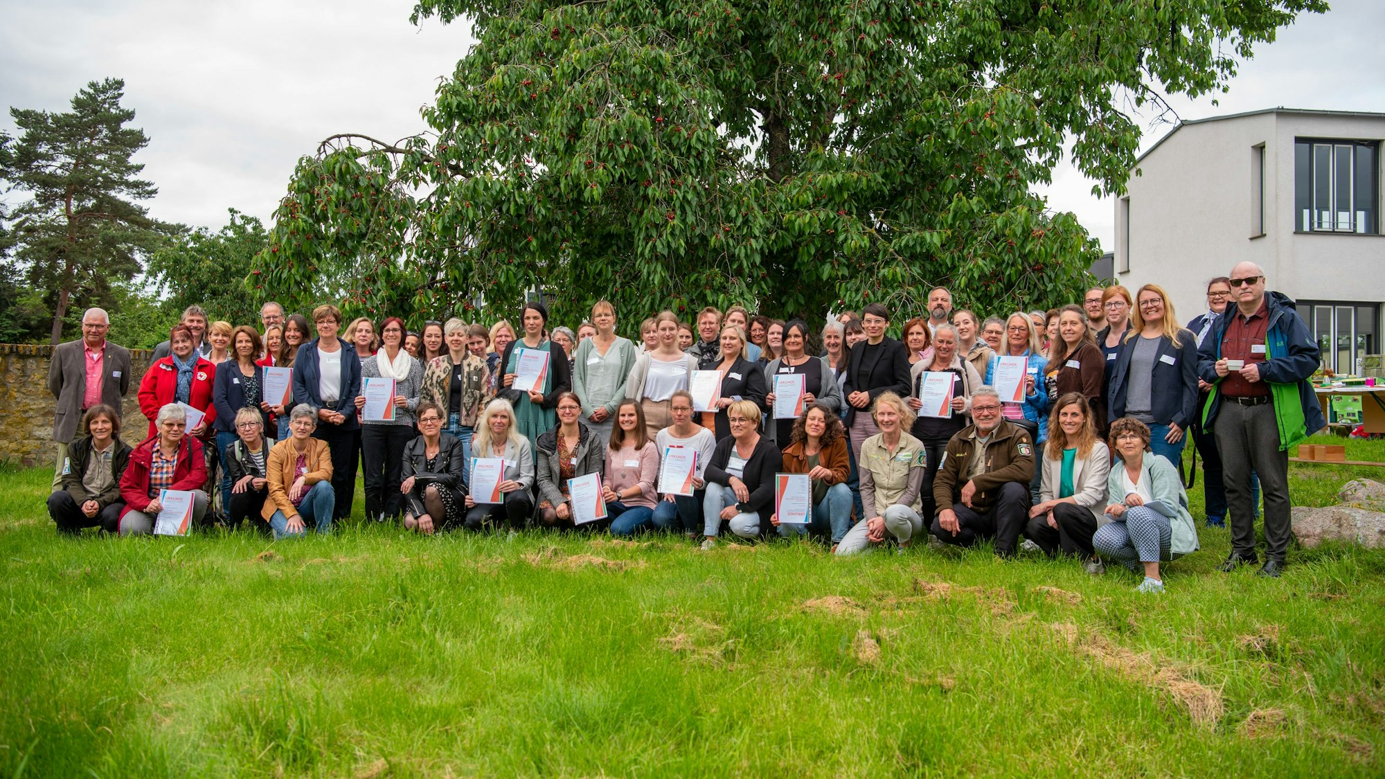 Eine Gruppe von Menschen steht auf einer Wiese unter einem Kirschbaum, mit dabei Josefine Paul (Grüne) Landesministerin für Kinder, Jugend, Familie, Gleichstellung, Flucht und Integration.