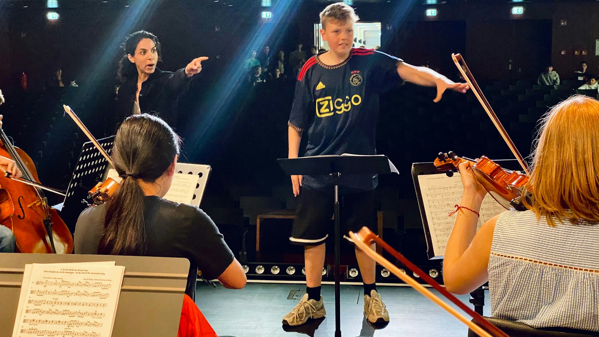 Eine Dirigentin und ein Schüler leiten ein Orchester an.