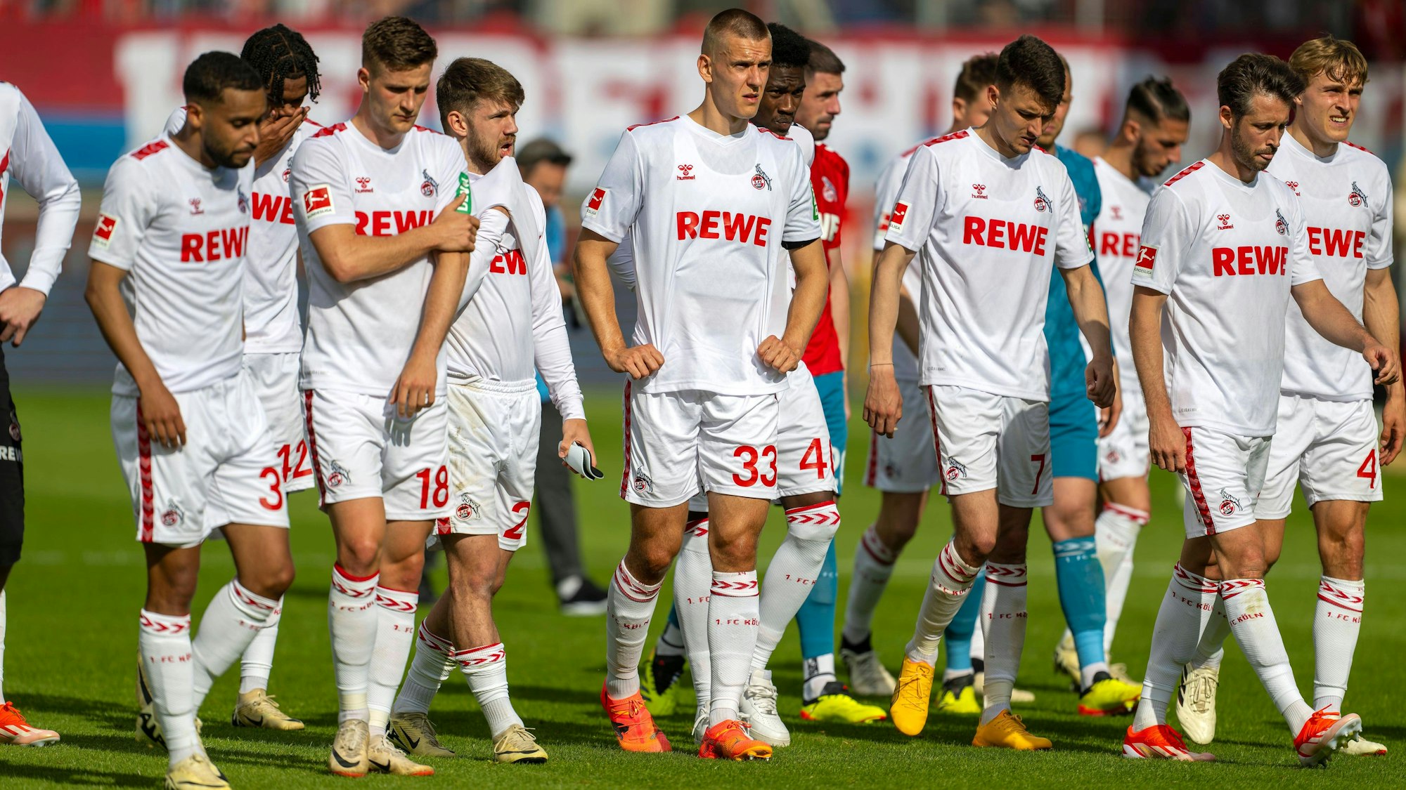 Die Mannschaft des 1. FC Köln geht resigniert über den Stadionrasen, nachdem sie das Match gegen den 1. FC Heidenheim verloren hat und in die Zweite Liga abgestiegen ist.
