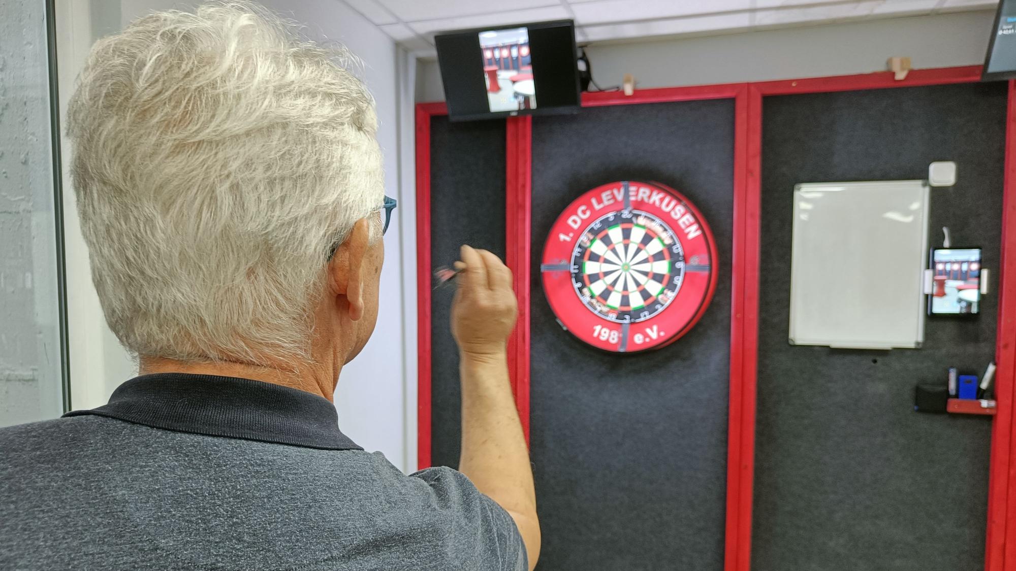 Ein Mann setzt zum Wurf eines Darts auf eine Scheibe an.