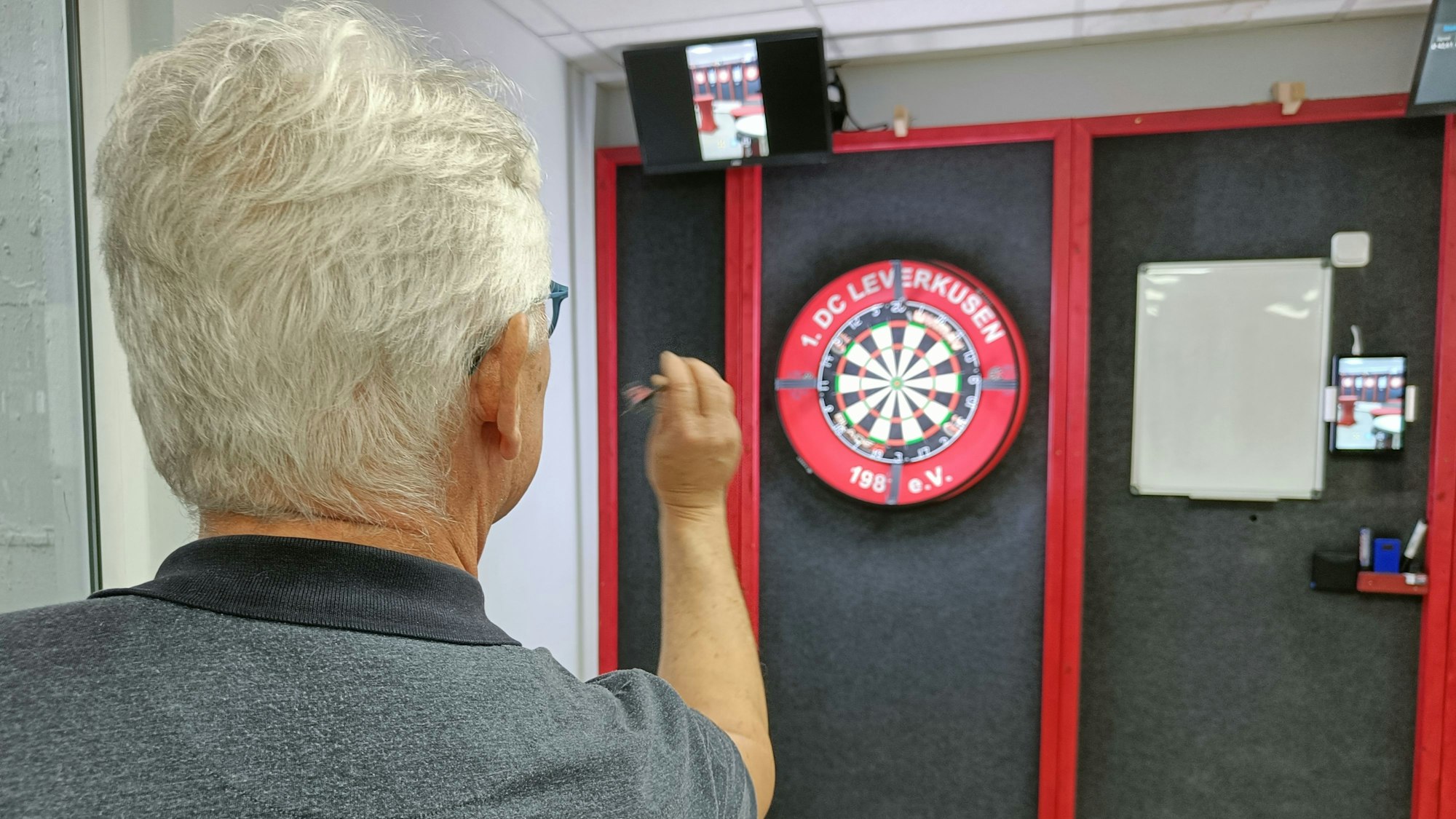 Ein Mann setzt zum Wurf eines Darts auf eine Scheibe an.