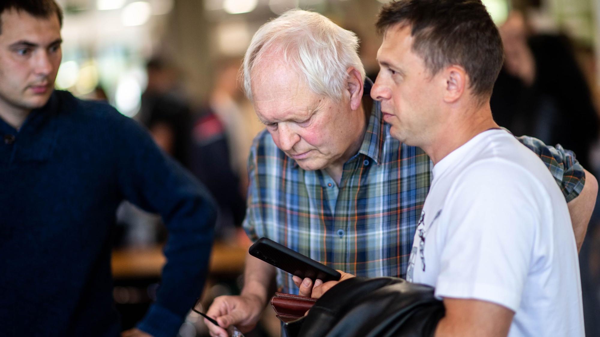 Das Bild zeigt Hans-Jürgen Lammers, wie auf das Smartphone eines Job-Suchenden schaut.