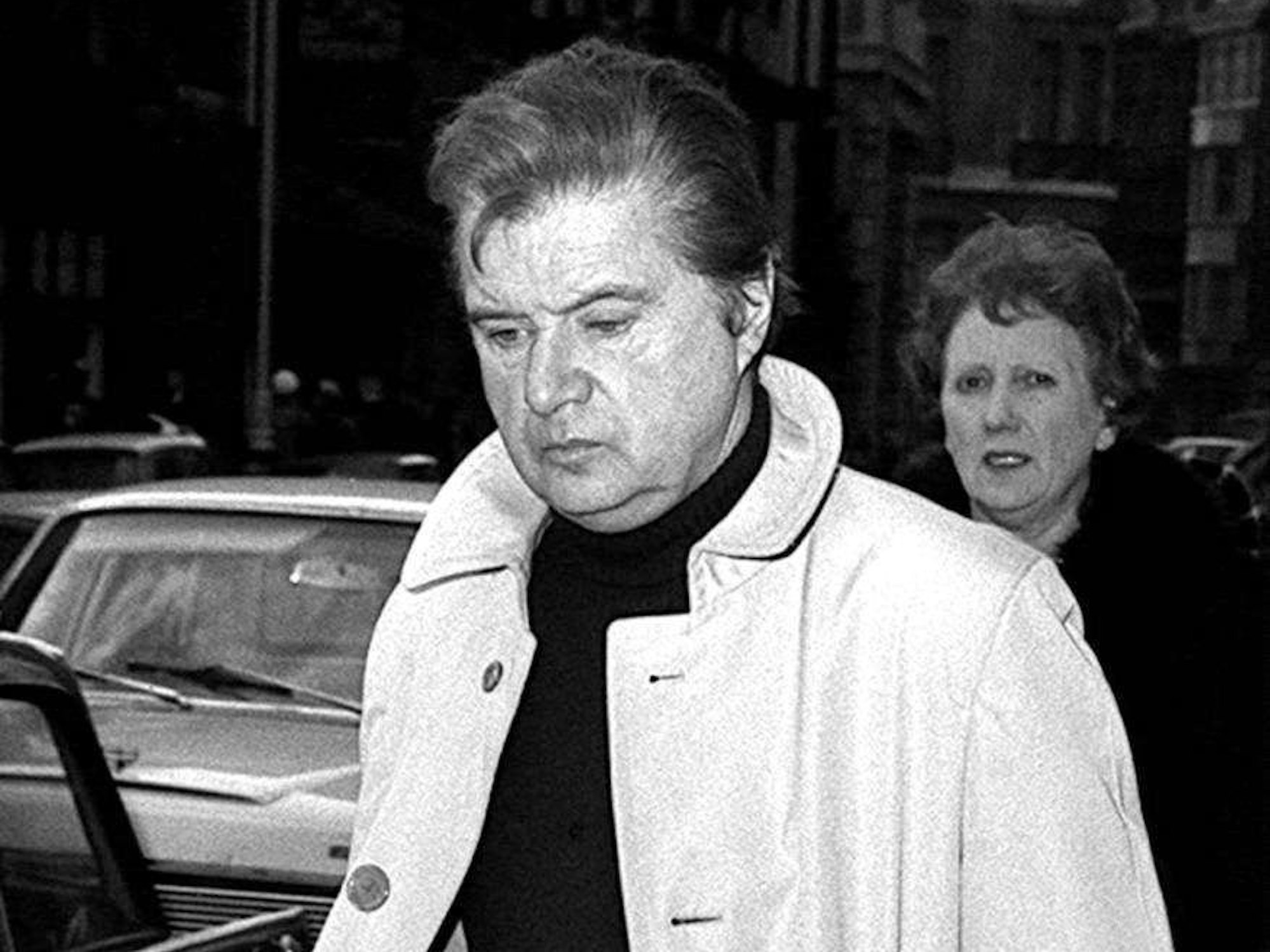 Großbritannien, London: Der Maler Francis Bacon trägt einen Mantel und blickt auf die Erde. Schwarz-weiße Aufnahme.