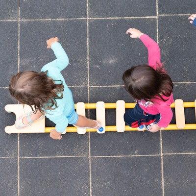 Kinder balancieren auf dem Spielplatz einer Kindertagesstätte auf einer Leiter.