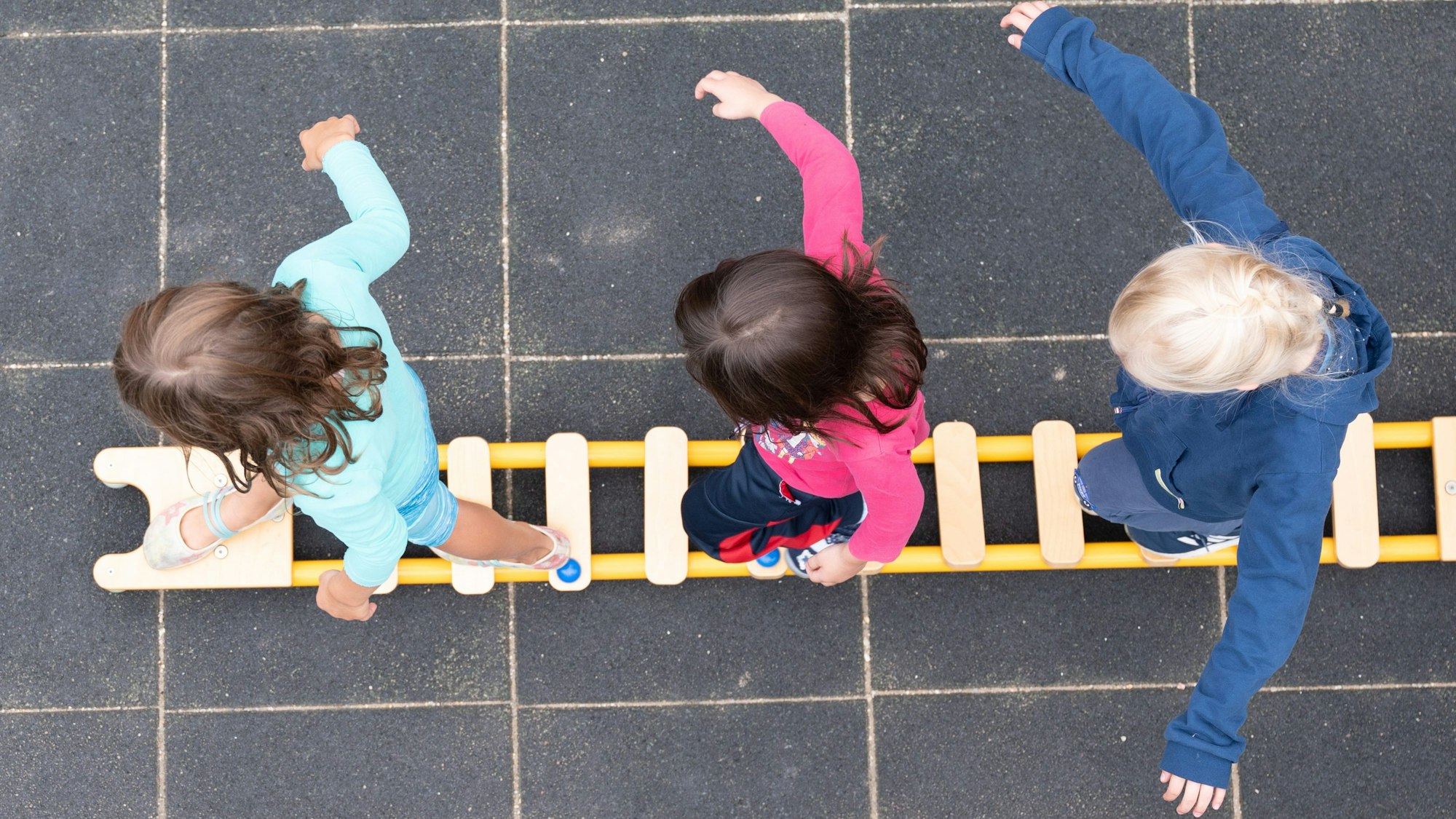 Kinder balancieren auf dem Spielplatz einer Kindertagesstätte auf einer Leiter.