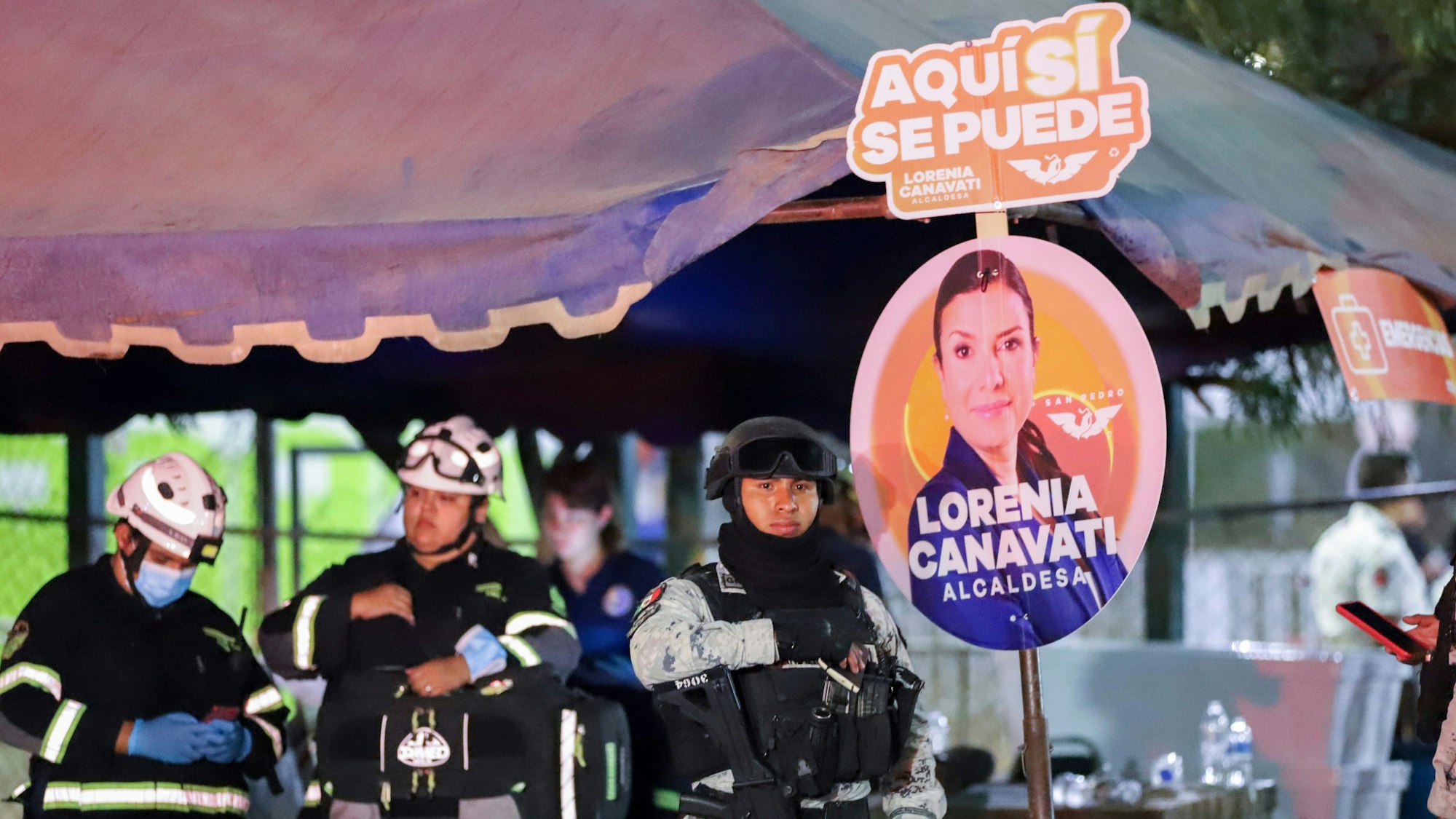 23.05.2024, Mexiko, San Pedro Garza Garcia: Hilfskräfte und Sicherheitskräfte stehen neben Wahlplakaten.