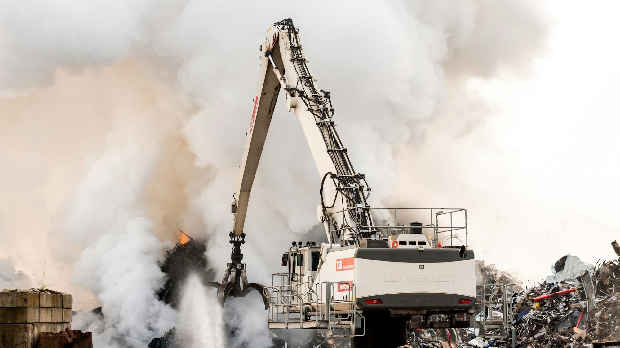 23.05.2024, Hamburg: Feuerwehrleute löschen im Stadtteil Harburg einen brennenden Schrotthaufen.