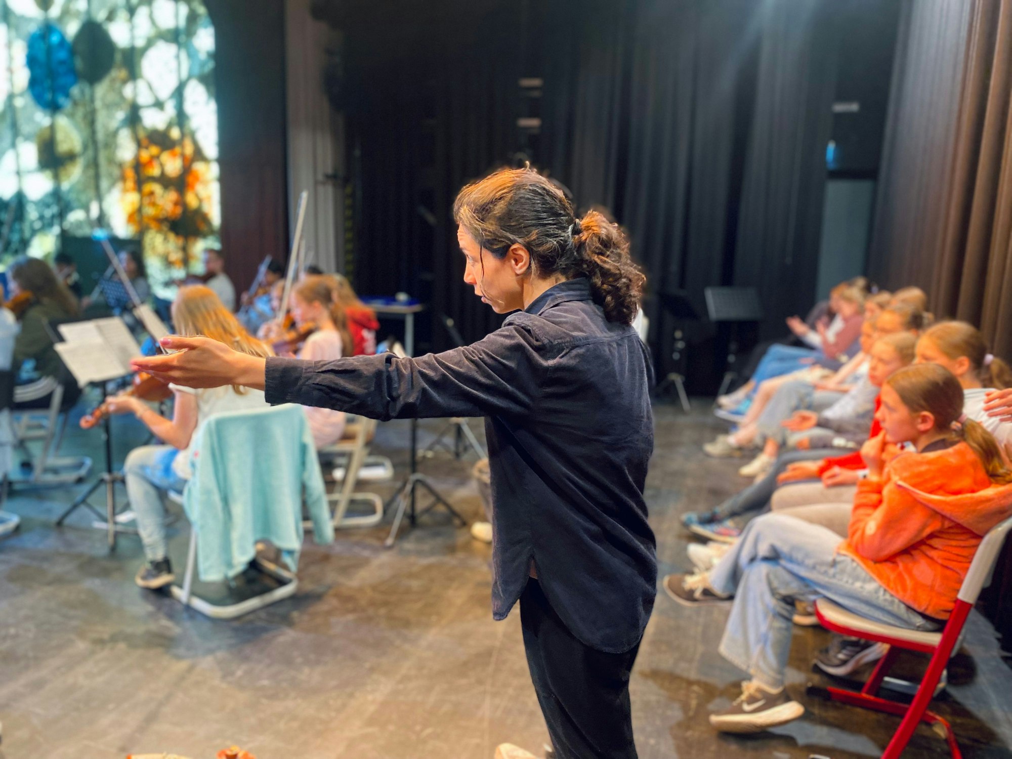 Bar Avni steht hinter dem Orchester, ihre Hand ist nach vorne ausgestreckt.