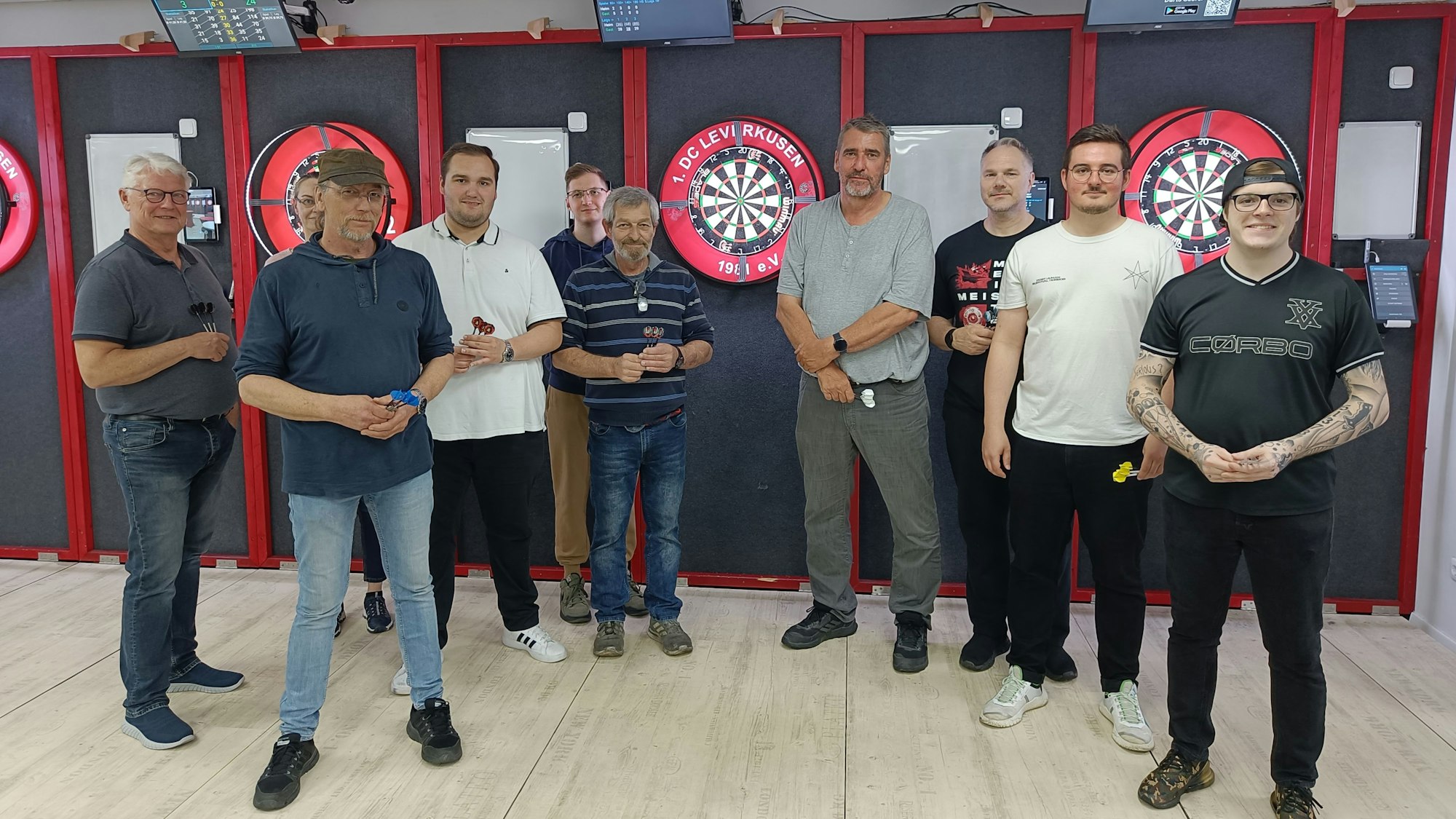 Neun Sportlerinnen und Sportler posieren vor Dartscheiben für ein Foto.