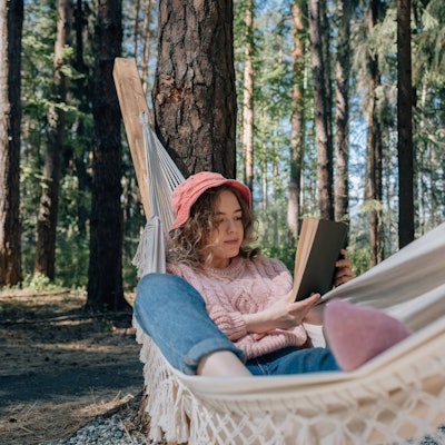 Junge Frau liegt in einer Hängematte und liest ein Buch. Symbolbild
