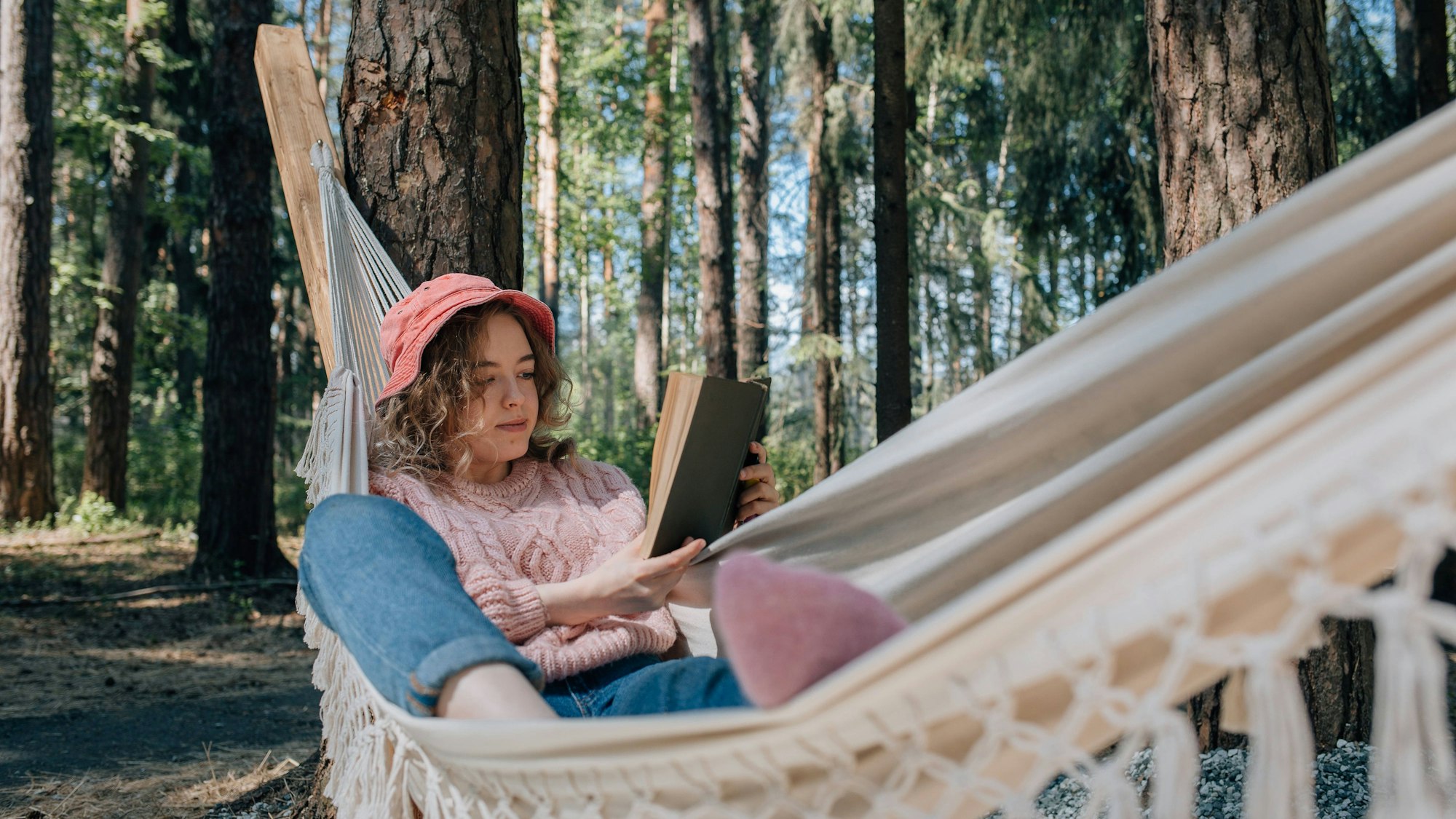Junge Frau liegt in einer Hängematte und liest ein Buch. Symbolbild