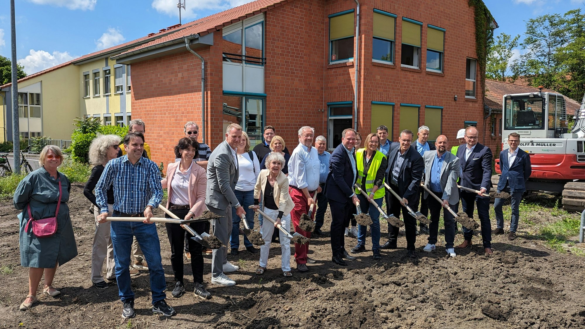 Eine große Gruppe von Männern und Frauen mit Spaten auf der Baustelle vor dem Altbau der Friedrich-Ebert-Realschule.
