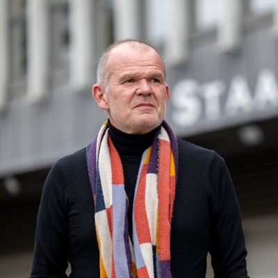 Francois-Xavier Roth, Generalmusikdirektor der Stadt Köln, steht vor dem Staatenhaus. Er trägt eine dunkle Jacke und einen gemusterten Schal.