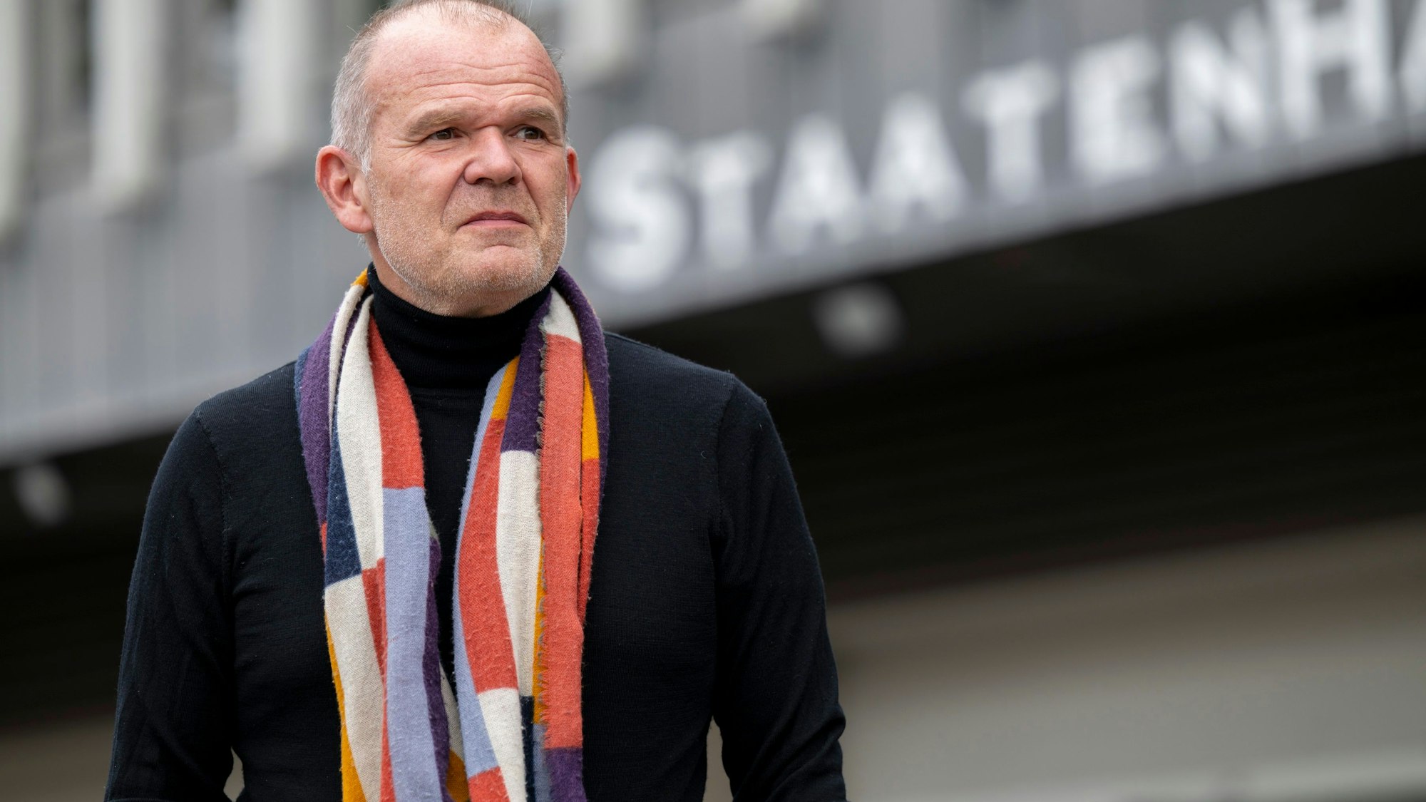 Francois-Xavier Roth, Generalmusikdirektor der Stadt Köln, steht vor dem Staatenhaus. Er trägt eine dunkle Jacke und einen gemusterten Schal.
