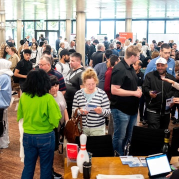 Zahlreiche Frauen und Männer stehen in einem Foyer, andere sitzen an Tischen.