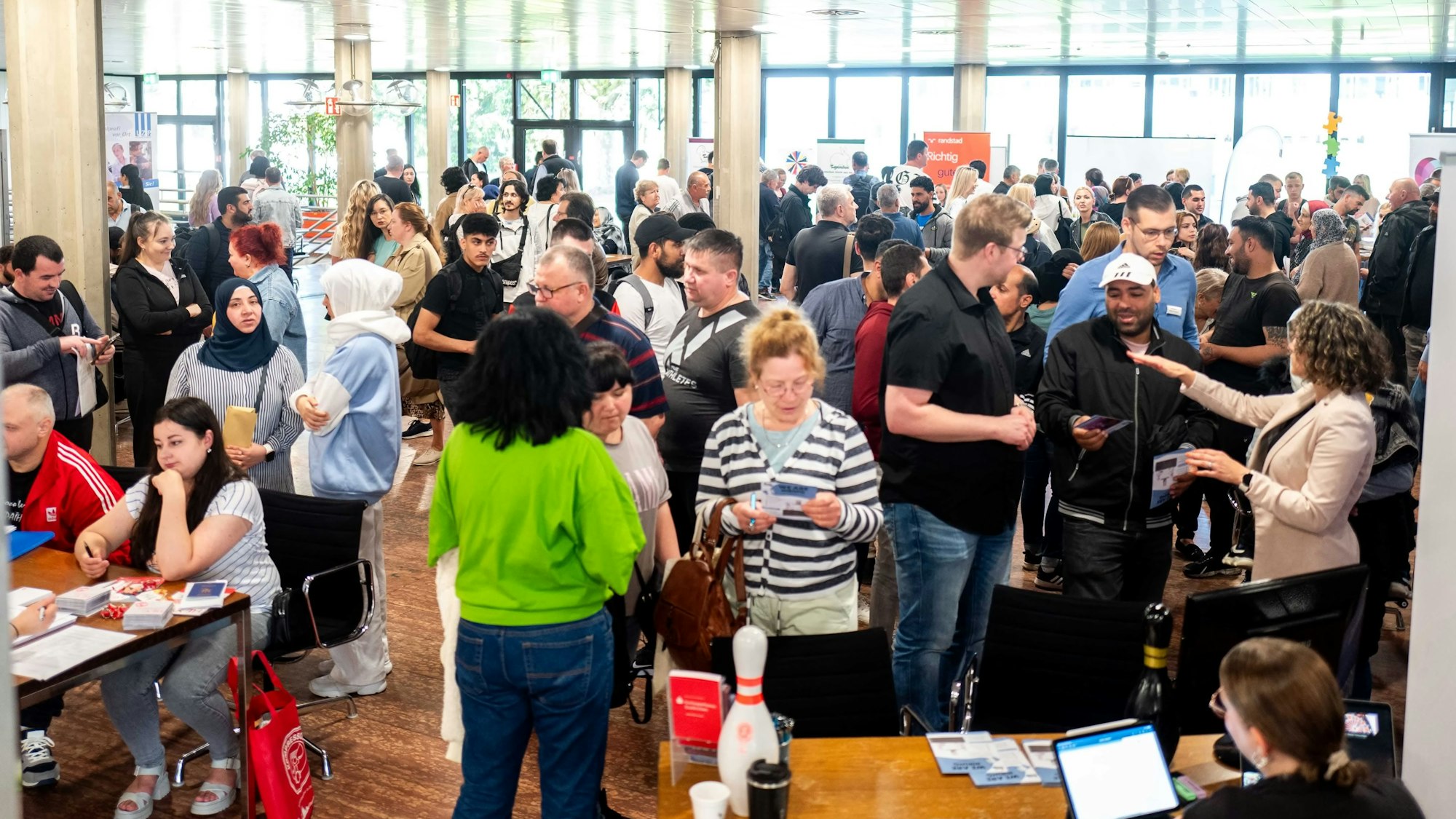 Zahlreiche Frauen und Männer stehen in einem Foyer, andere sitzen an Tischen.