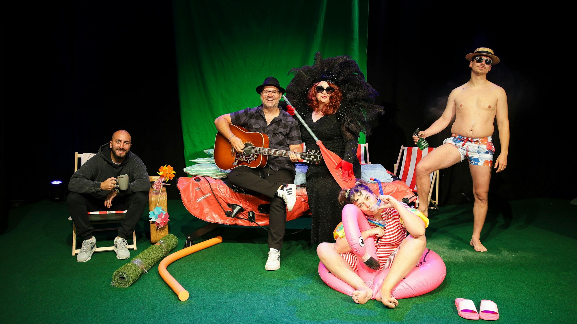 Fünf Menschen sitzen und stehen in einer Kulisse mit Badesachen.