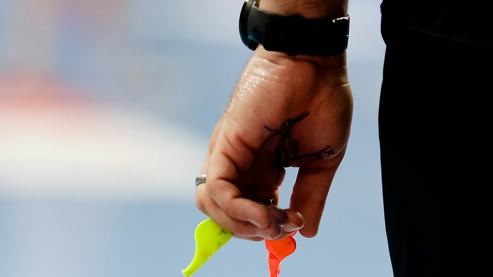 Ein Schiedsrichter hält zwei Pfeifen in der Hand.