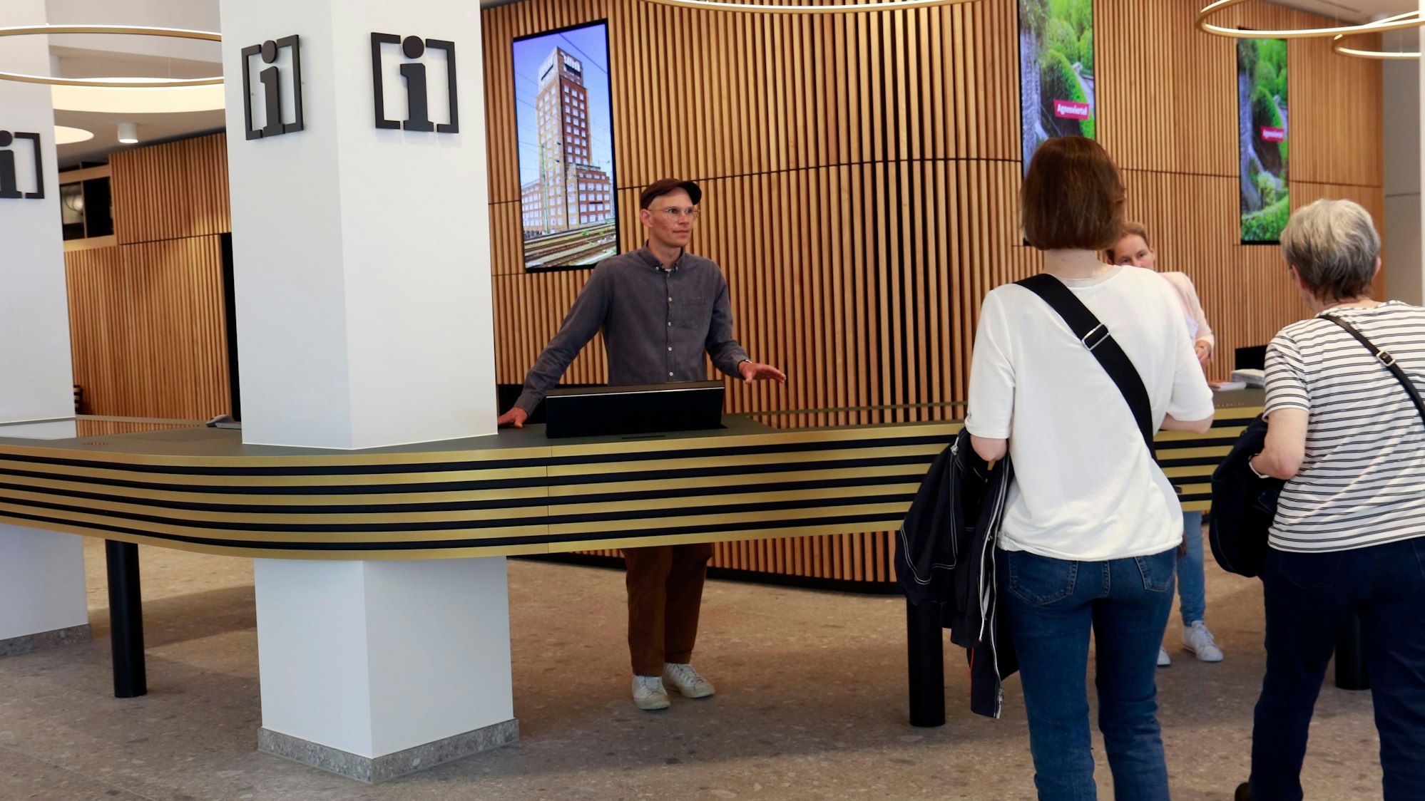 Zwei Menschen bedienen Touristen an einer Touristen-Info.