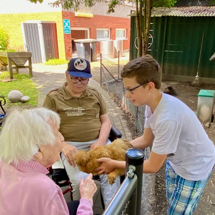 Zu sehen sind zwei Senioren und ein Junge, die eines der Hühner streicheln.