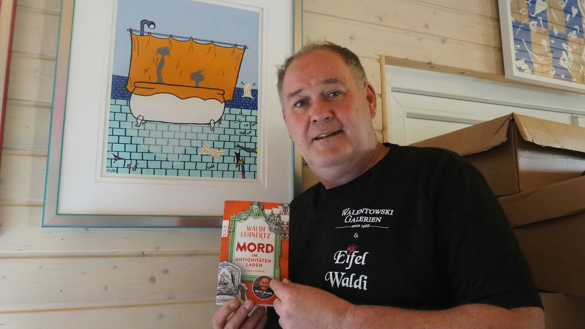 Walter Lehnertz steht mit seinem Buch vor einem seiner Bilder.