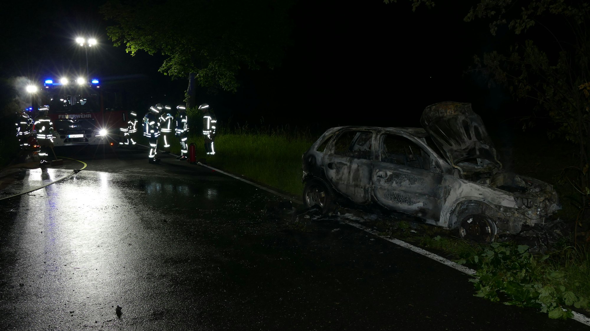 Feuerwehrleute stehen vor einem ausgebrannten Auto.