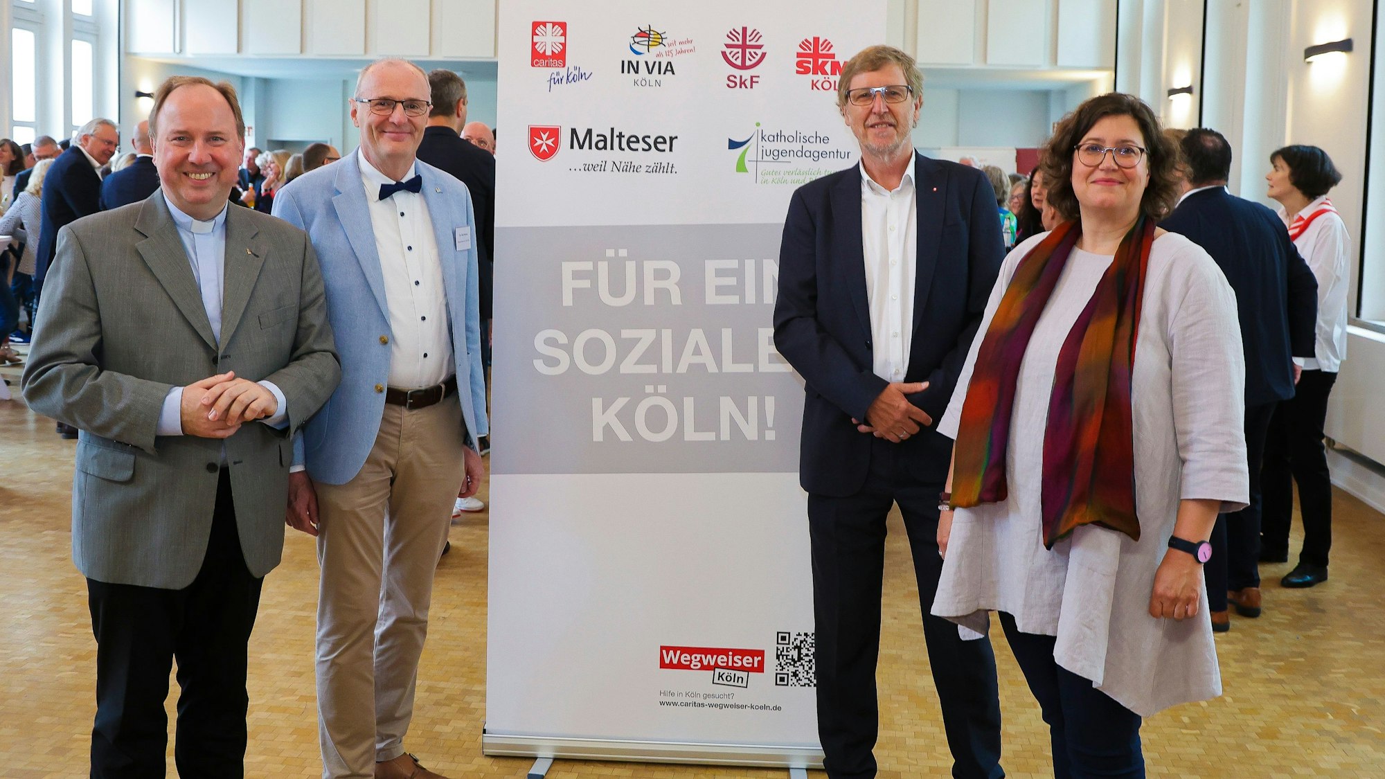Zu sehen sind vier Menschen, die vor einem Aufsteller mit dem Satz „Für ein soziales Köln“ stehen.