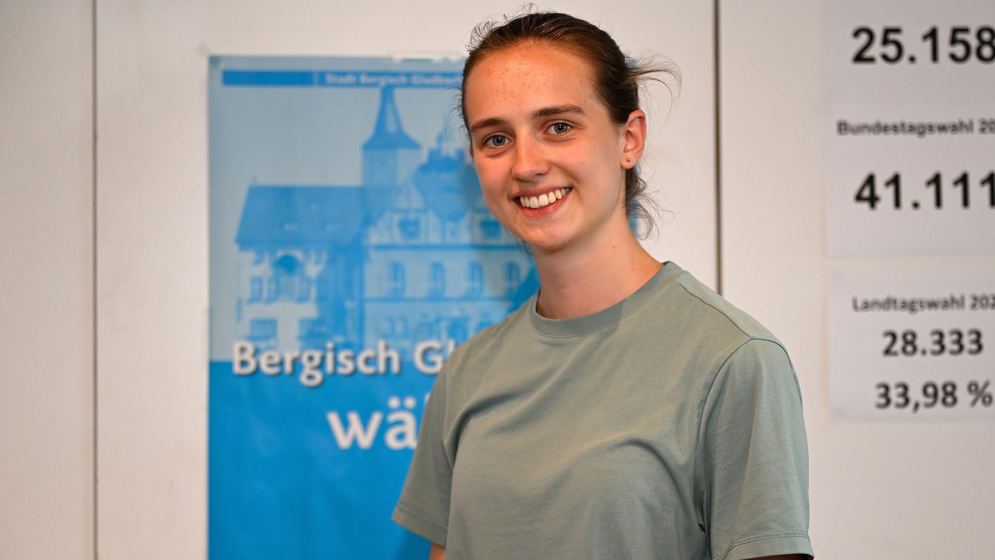 Porträtfoto von Anne Stößel vor dem Hintergrund eines Plakats zur Europawahl.