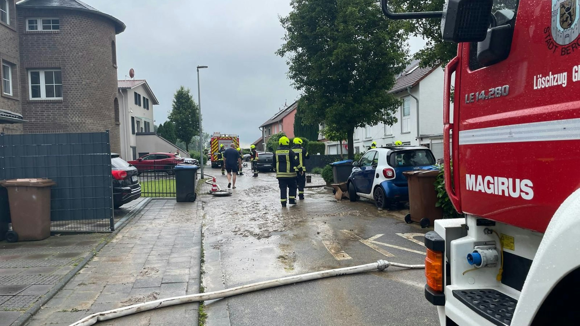 Feuerwehrleute stehen auf einer von Schlamm überspülten Straße in Büsdorf.
