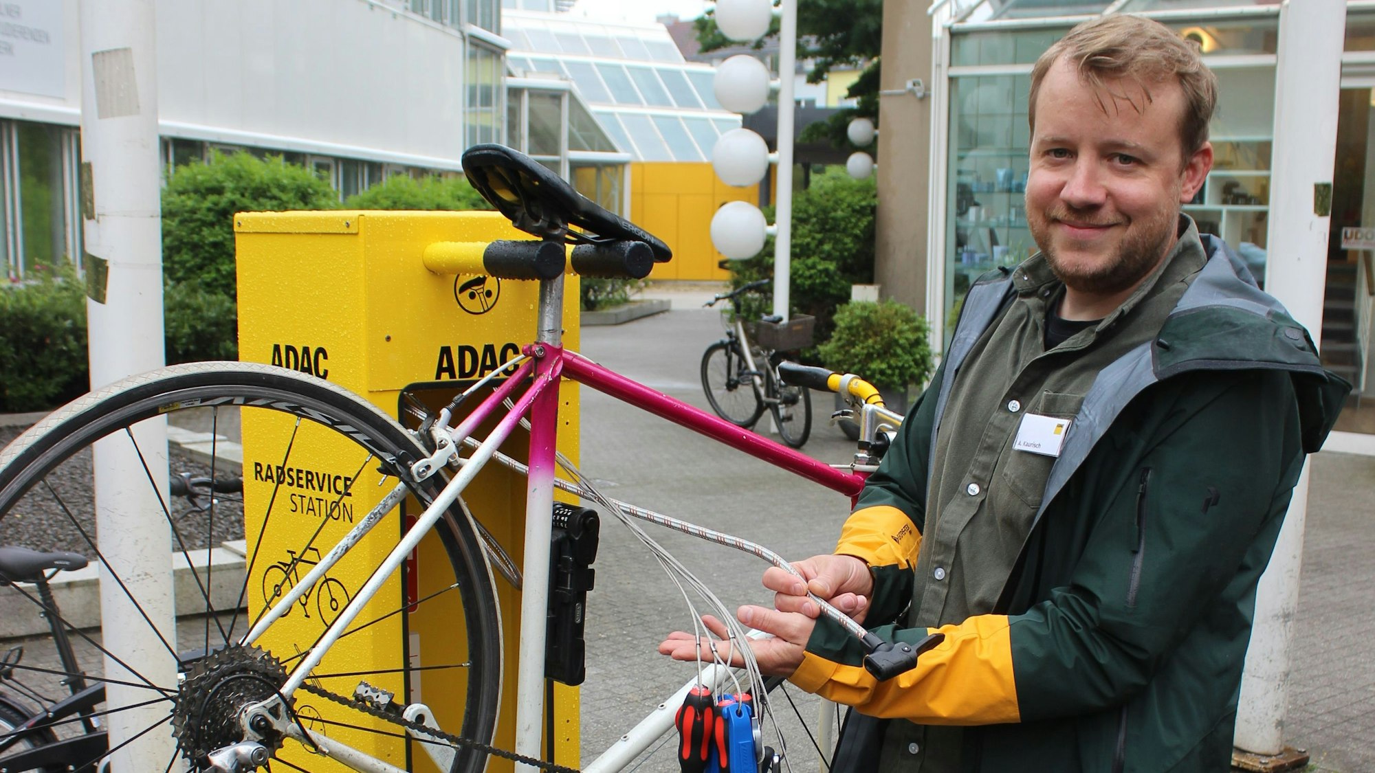 Zu sehen ist ein Mann, der verschiedene Werkzeuge, wie zum Beispiel Inbus-Schlüssel und Schraubendreher, die für eine Fahrrad-Reparatur benötigt werden, in den Händen hält.