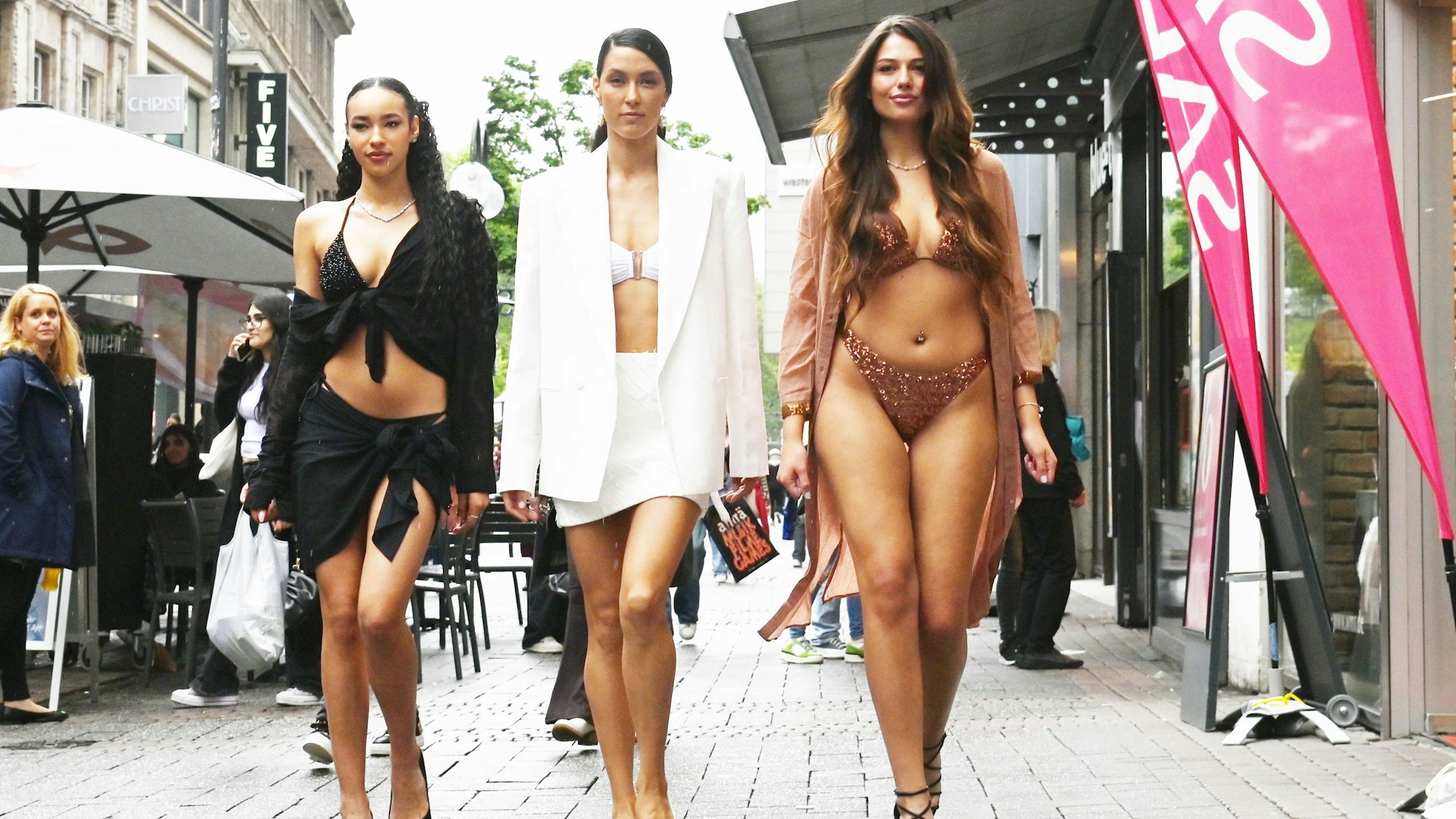 Drei Frauen laufen in Bademode durch eine Einkaufsstraße.