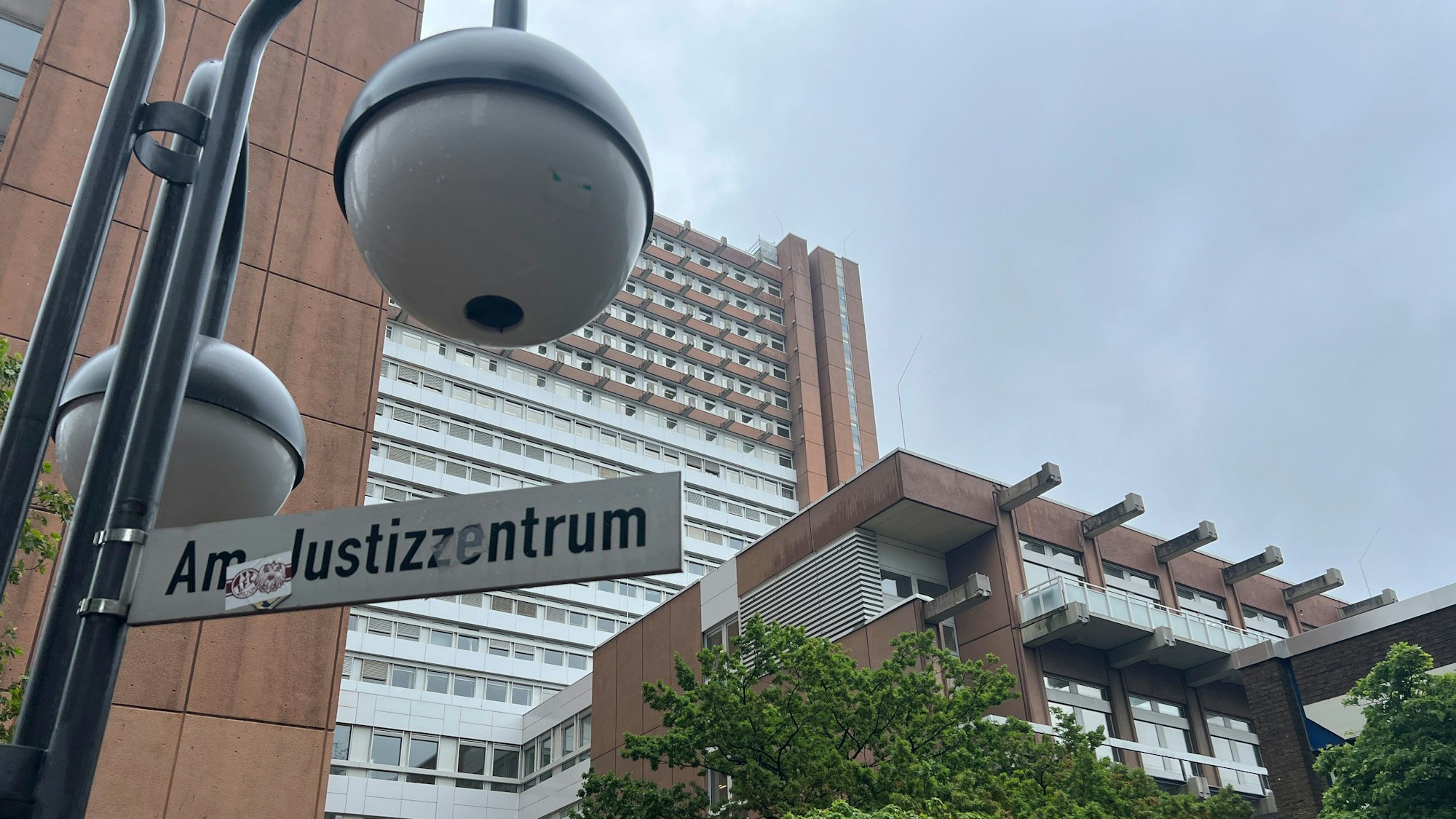 Auf einem Straßenschild vor einem großen Gebäude steht: „Am Justizzentrum“.