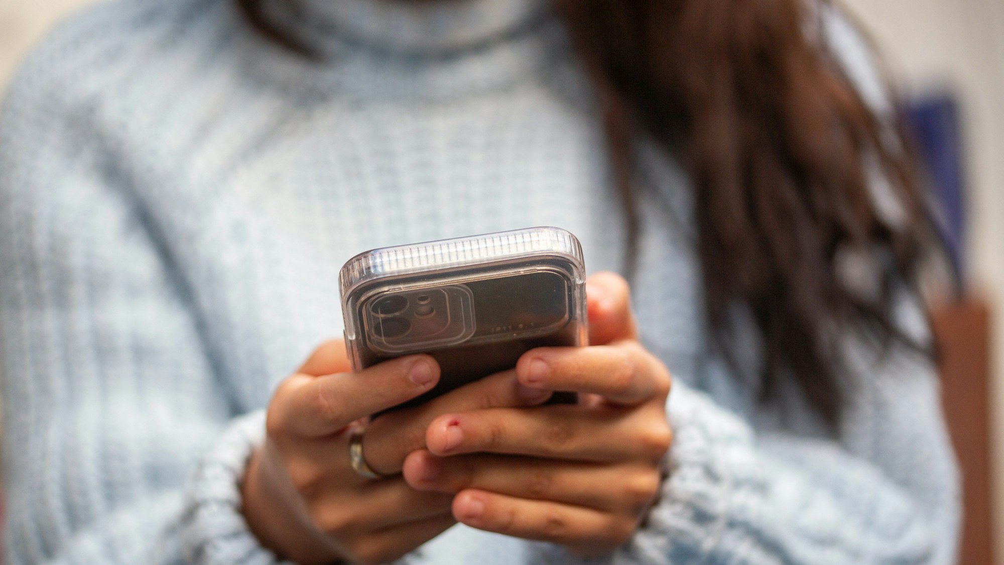 Eine junge Frau hält ein Smartphone in den Händen.