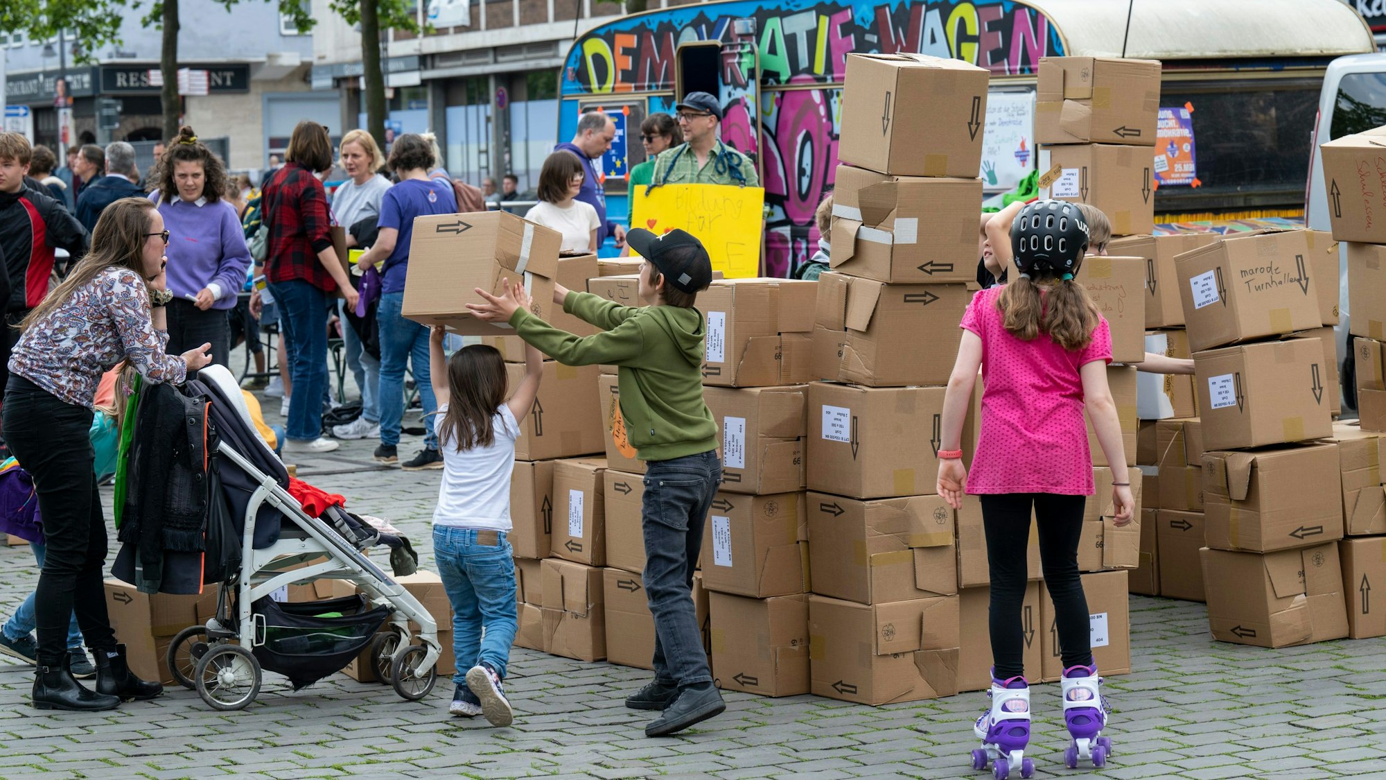 Unter dem Motto „Bildung braucht Demokratie“ protestieren Eltern und Kinder auf dem Heumarkt. Sie stapeln gemeinsam Kartons.