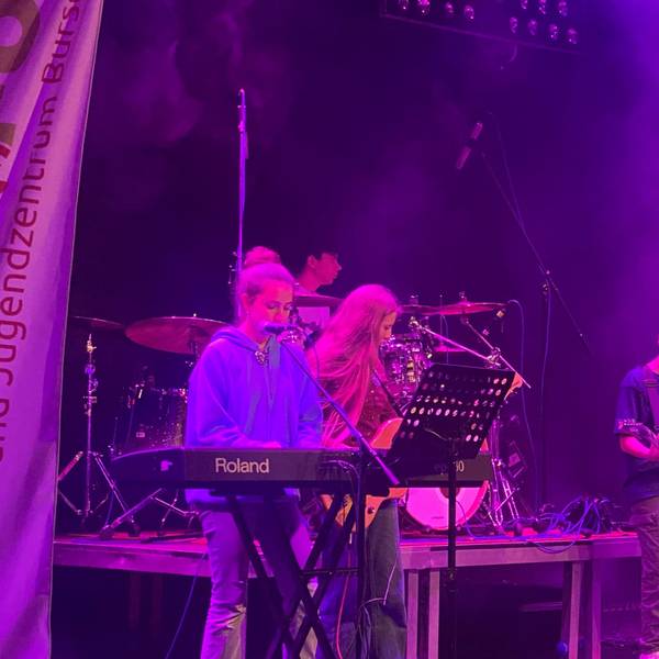 Ein Band mit Jugendlichen steht auf einer Bühne und macht Musik.