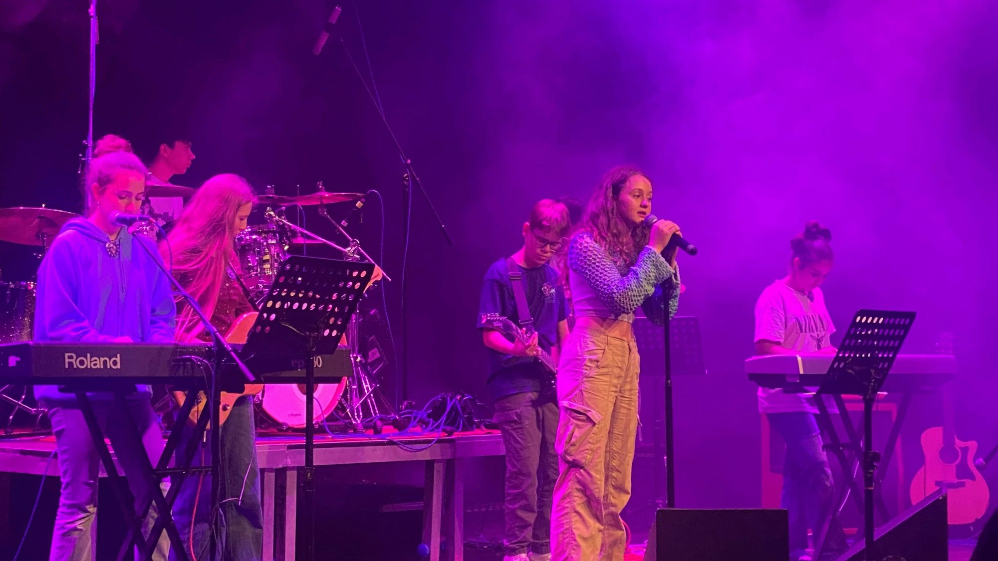 Ein Band mit Jugendlichen steht auf einer Bühne und macht Musik.