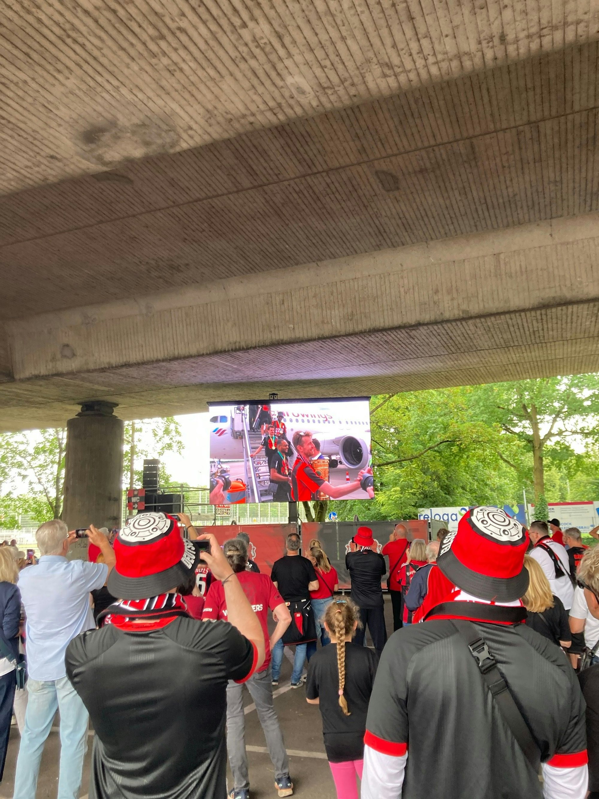 Gebannt verfolgen die Fans auf der Fanmeile die Ankunft der Leverkusener Mannschaft auf den aufgestellten Leinwänden. Als Kapitän Lukas Hradecky das Flugzeug mit Pokal und Meisterschale in der Hand verlässt, brandet tosender Jubel auf.