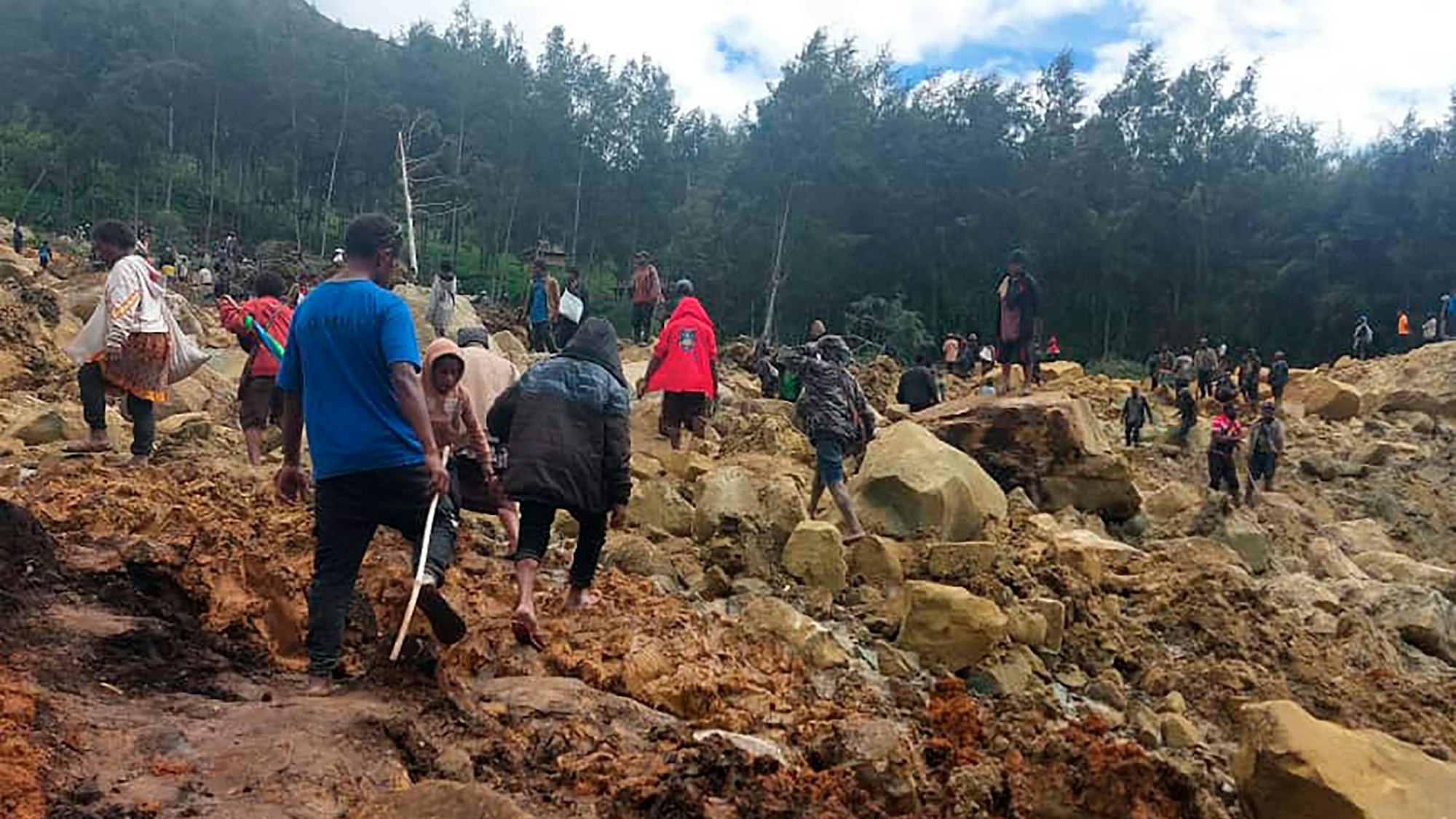 HANDOUT - 24.05.2024, Papua-Neuguinea, Yambali: Auf diesem von der Internationalen Organisation für Migration via AP zur Verfügung gestellten Foto überqueren Menschen den Bereich des Erdrutsches, um auf die andere Seite zu gelangen. Nach einem Erdrutsch werden im abgelegenen Hochland Papua-Neuguineas Hunderte Tote befürchtet. Das Dorf Yambali etwa sei unter den Erdmassen verschwunden, beschrieb die örtliche Zeitung «Post Courier» das Unglück am Samstag. (Bestmögliche Qualität) Foto: Benjamin Sipa/International Organization for Migration/AP/dpa - ACHTUNG: Nur zur redaktionellen Verwendung im Zusammenhang mit der aktuellen Berichterstattung und nur mit vollständiger Nennung des vorstehenden Credits +++ dpa-Bildfunk +++