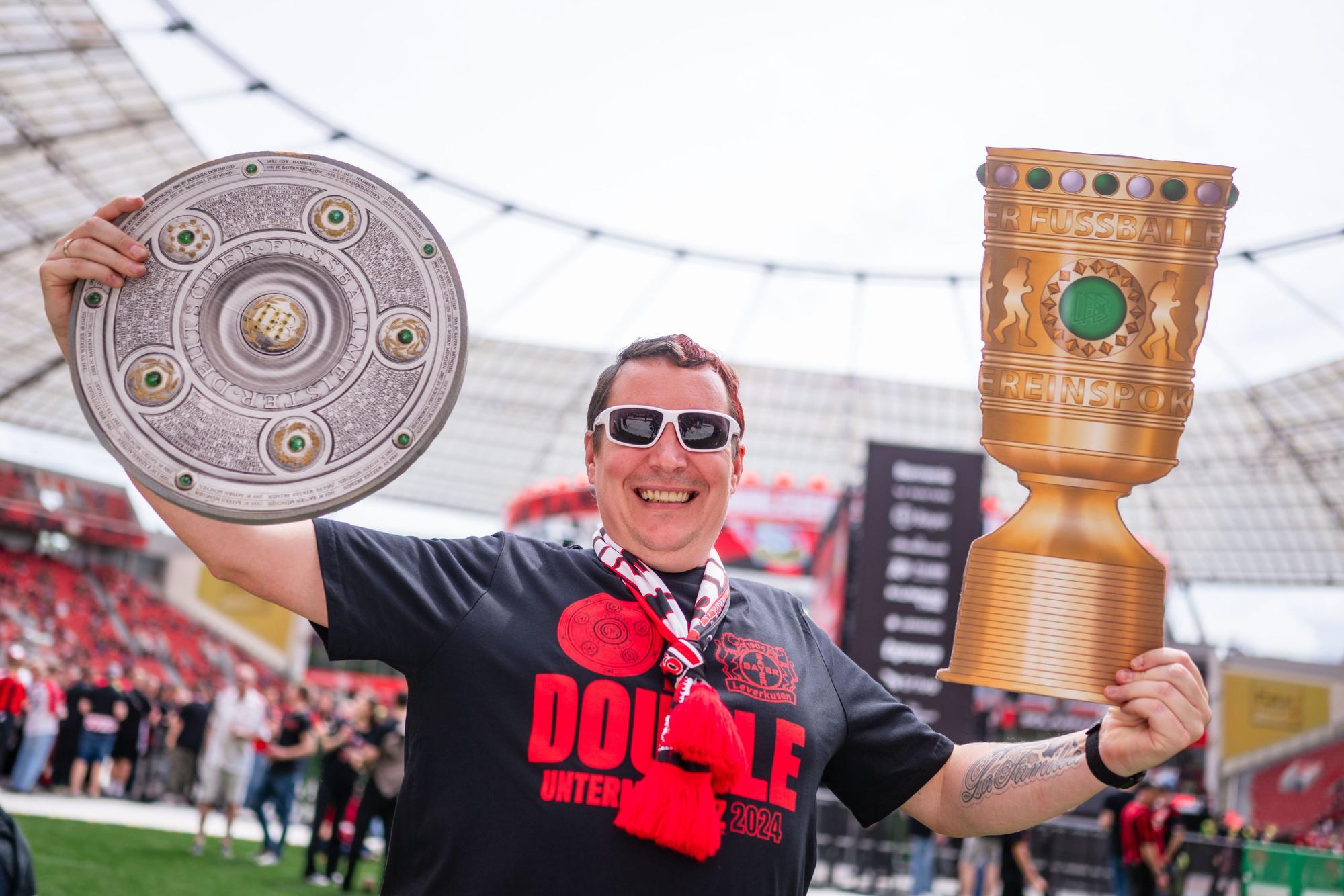 Fan Sasha wartet in der BayArena auf die Ankunft der Mannschaft von Bayer 04 Leverkusen und hält dabei eine Meisterschale (l) und einen DFB-Pokal in den Händen.