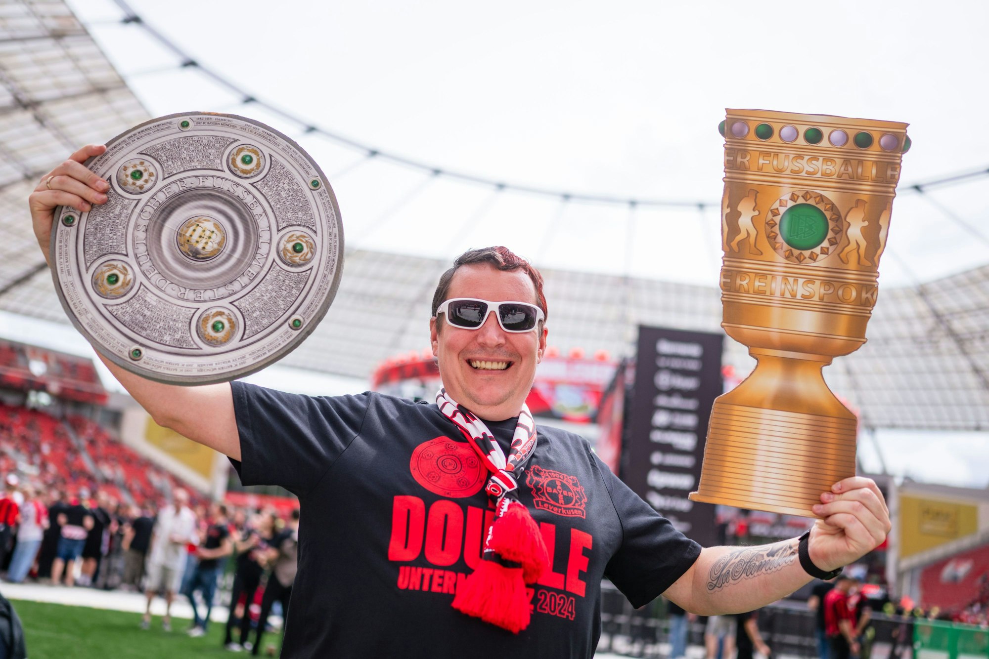 Fan Sasha wartet in der BayArena auf die Ankunft der Mannschaft von Bayer 04 Leverkusen und hält dabei eine Meisterschale (l) und einen DFB-Pokal in den Händen.